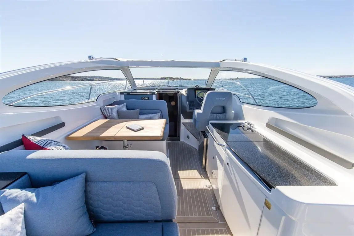 Modern boat interior with comfortable seating, a wooden table, kitchen area, and scenic views of the water outside.